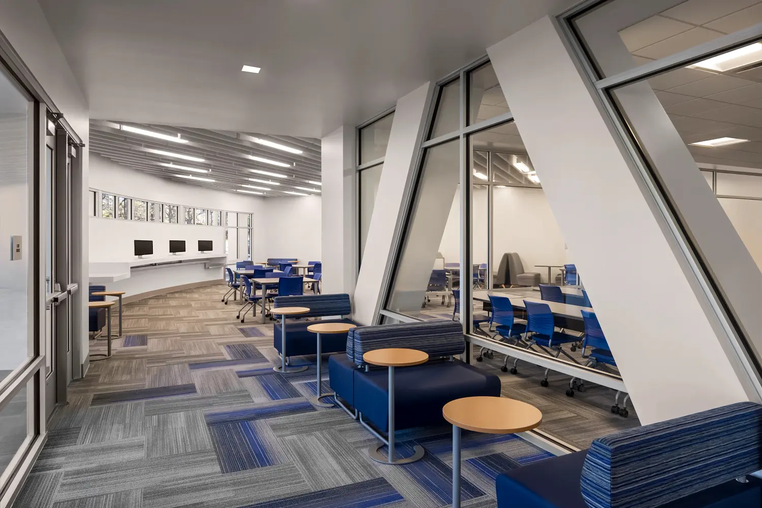 blue plush seating with round wooden desks lining a hallway in an educational building.