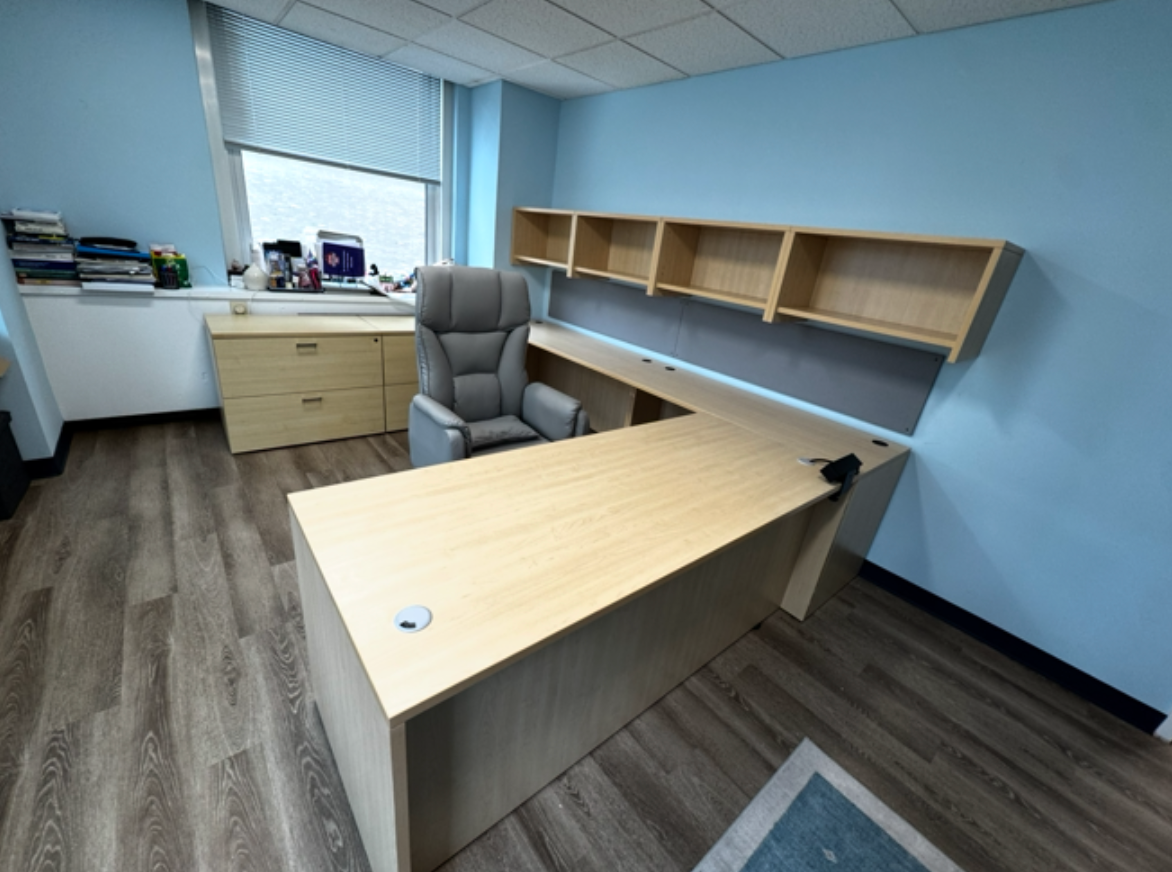an office with blue, light wood desk and gray ergonomic chair.